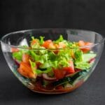 Glass bowl with vegetable salad on black background.