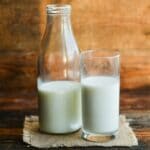 Glass bottle of milk with glass cup of milk on wooden table.