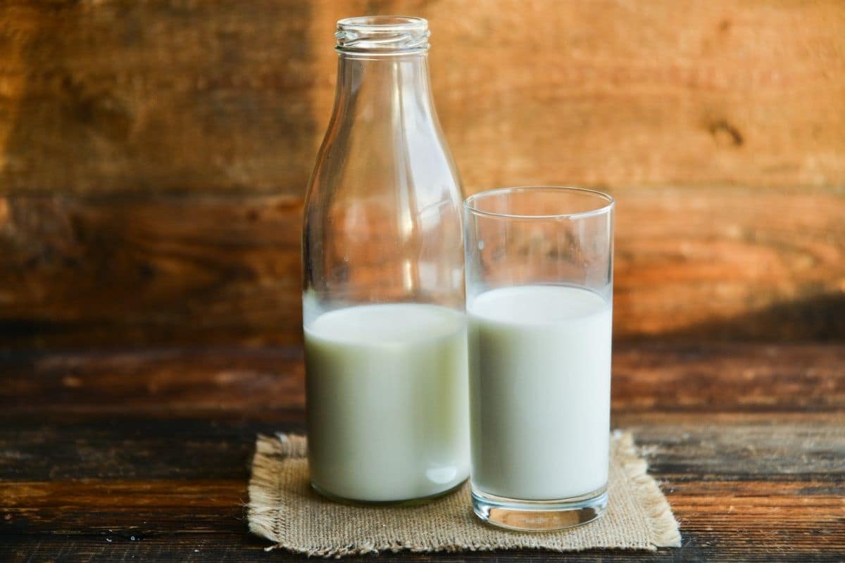 Glass bottle and glass cup of milk on wooden table.