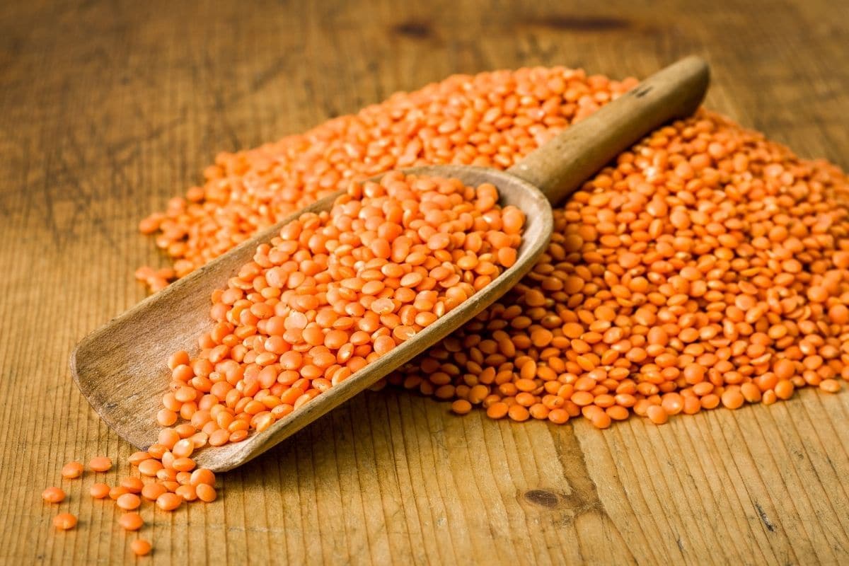 Pile of orange lentils on table with wooden spoon.