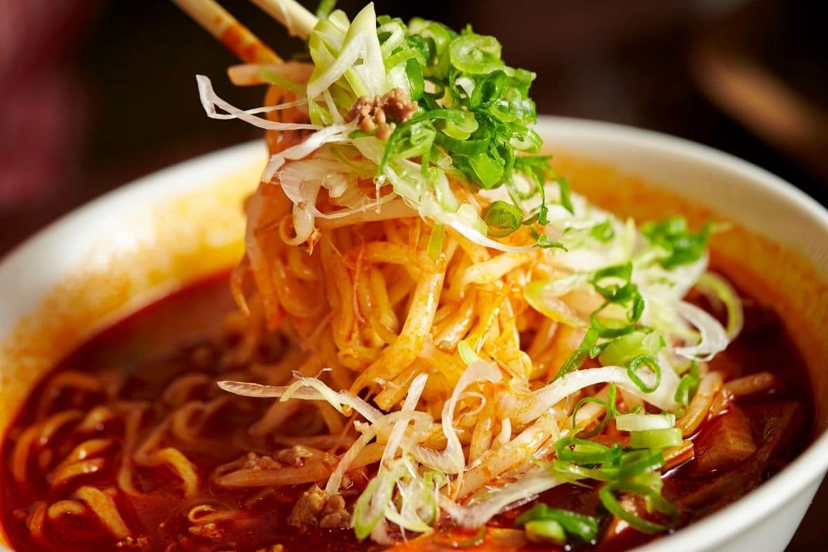 Spicy ramen noodles in white bowl picked by sticks.
