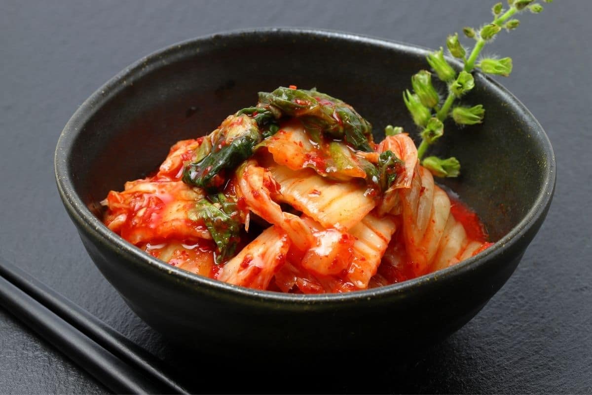 Black bowl of korean kimchi on black table.