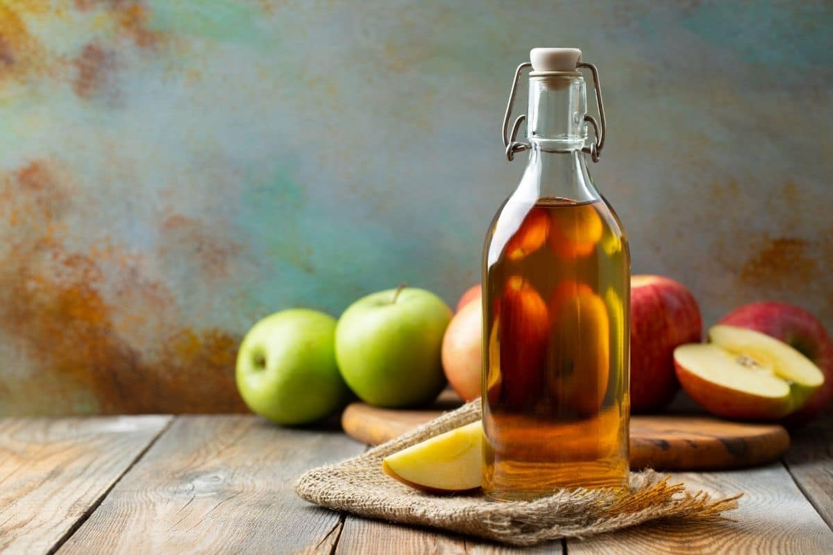Glass bottle of apple vinegar on table, Apples in the background.