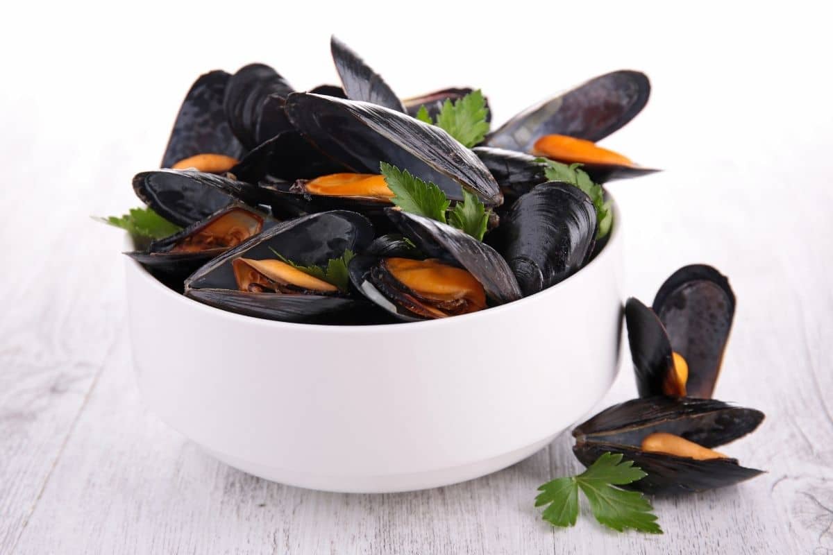 White bowl full of mussels on cream table.