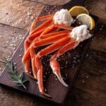 Fresh crab legs with herb, salt and lemon on wooden cutting board.