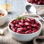 White bowl of red kidney beans on table with spoon.