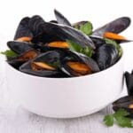 White bowl full of mussels on cream table.