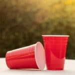 Two red solo cups on white table on sunny day.