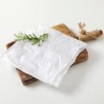 Was paper sheet with herb on wooden cutting board on white background.