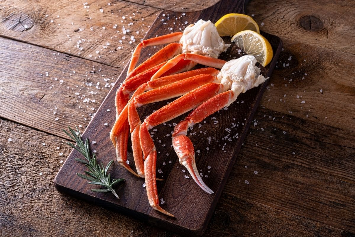 Fresh crab legs with herb, salt and lemon on wooden cutting board.