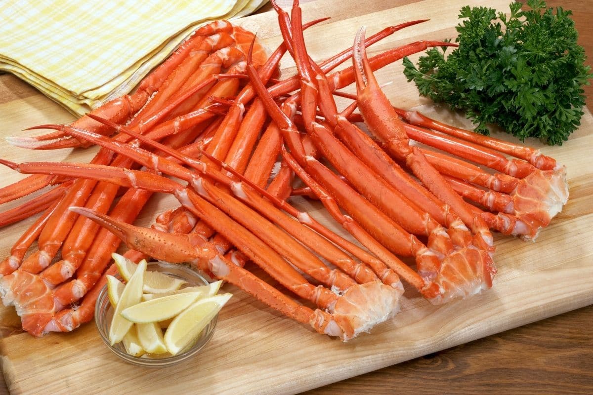 Spreaded crab legs with slices of lemon, herb on wooden cutting board.