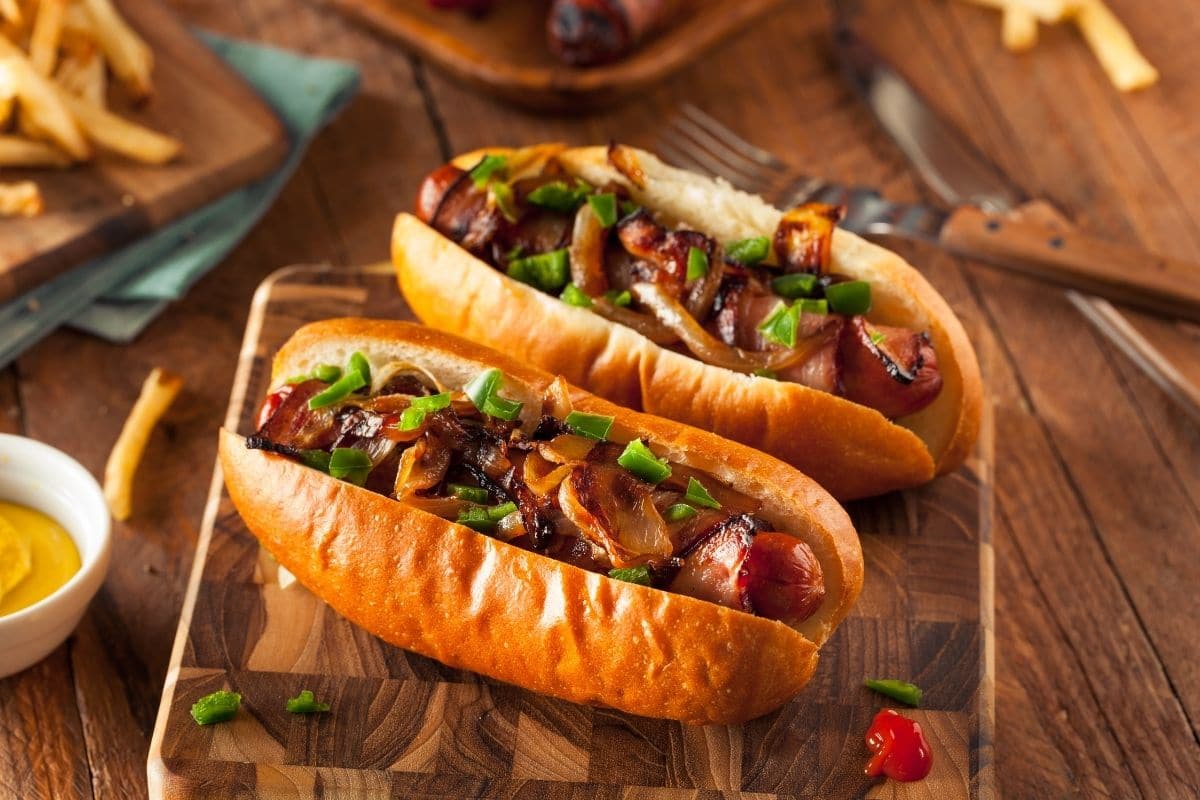 Homemade hot dogs with onion and peppers on wooden cutting board.