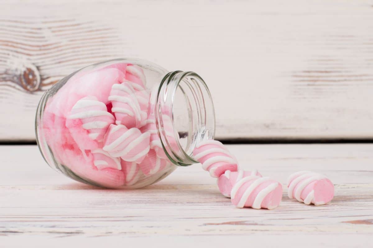 Vintage glass jar full of pink marshmallows spilling on table.