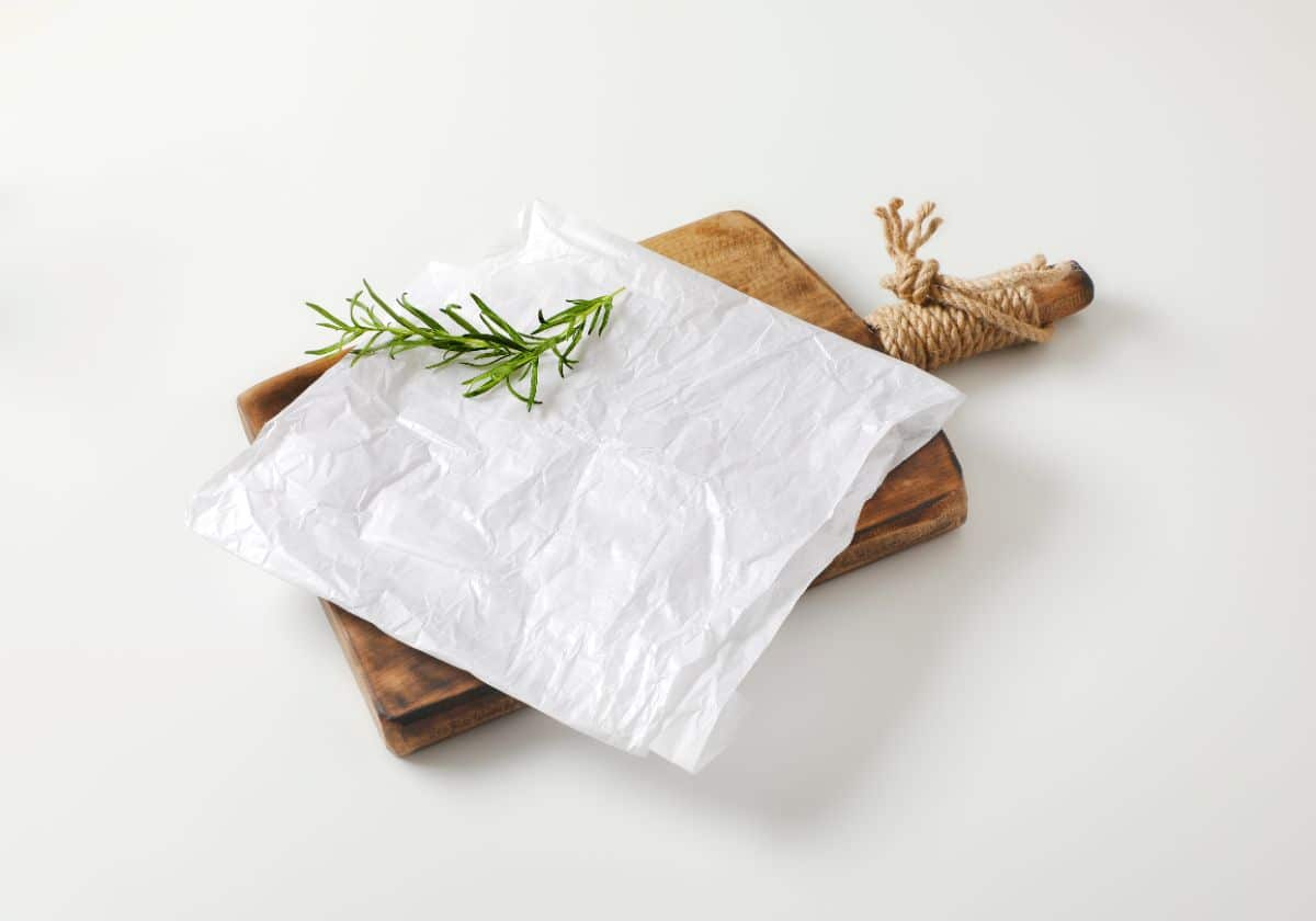 Was paper sheet on wooden cutting board with herb on white background.