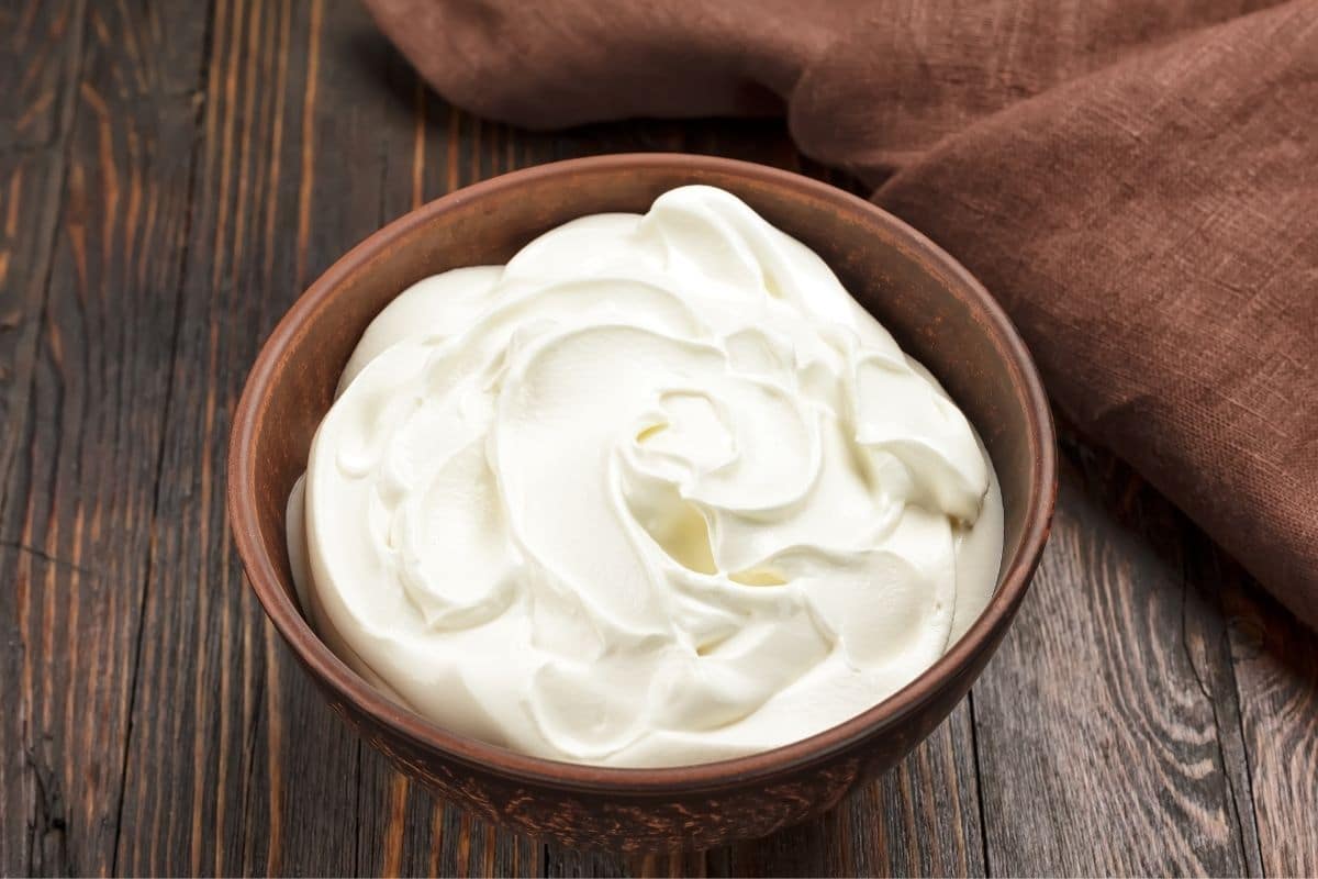 Wooden bowl of sour cream on wooden table.