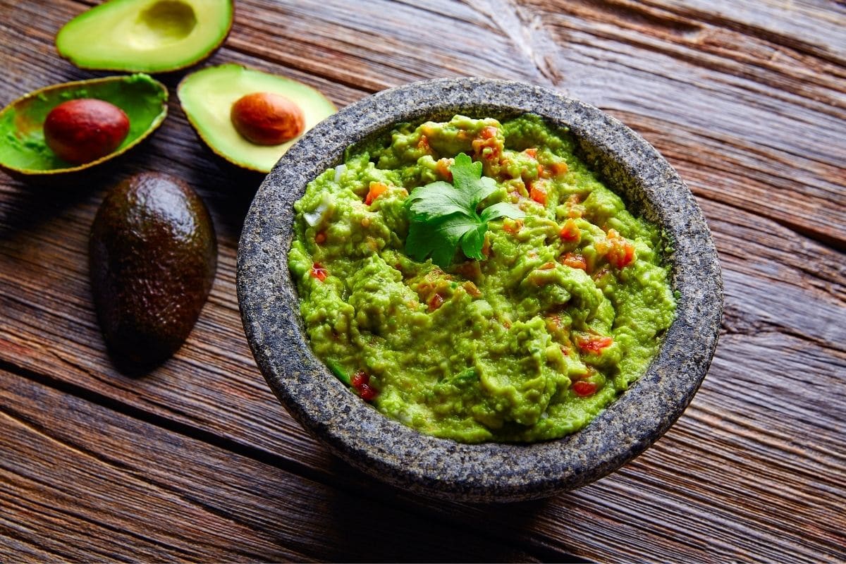 Stone bowl full of guacamole on table with avocado leftovers.