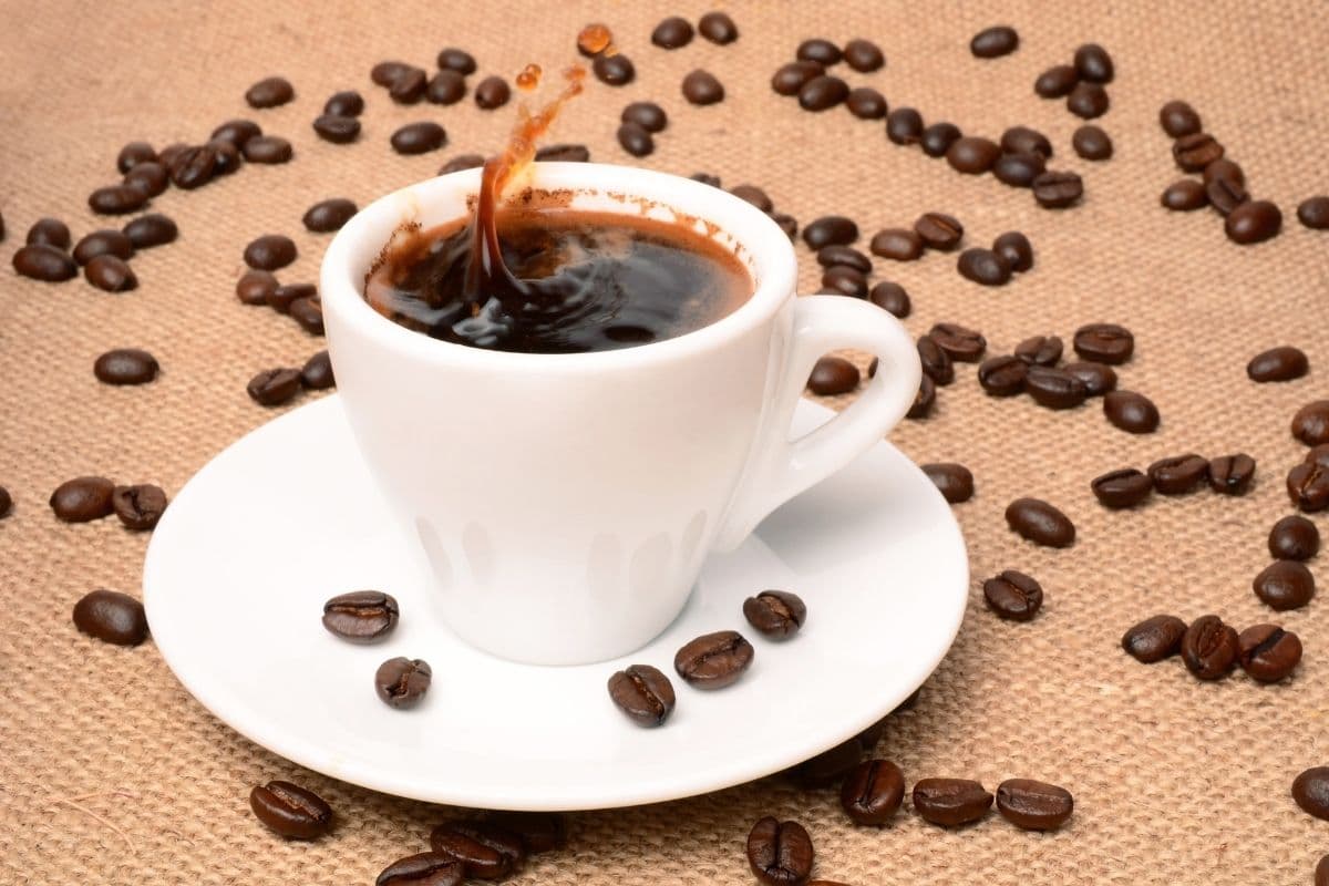 Cup of coffe on small plate on brown table with scattered coffe beans around.