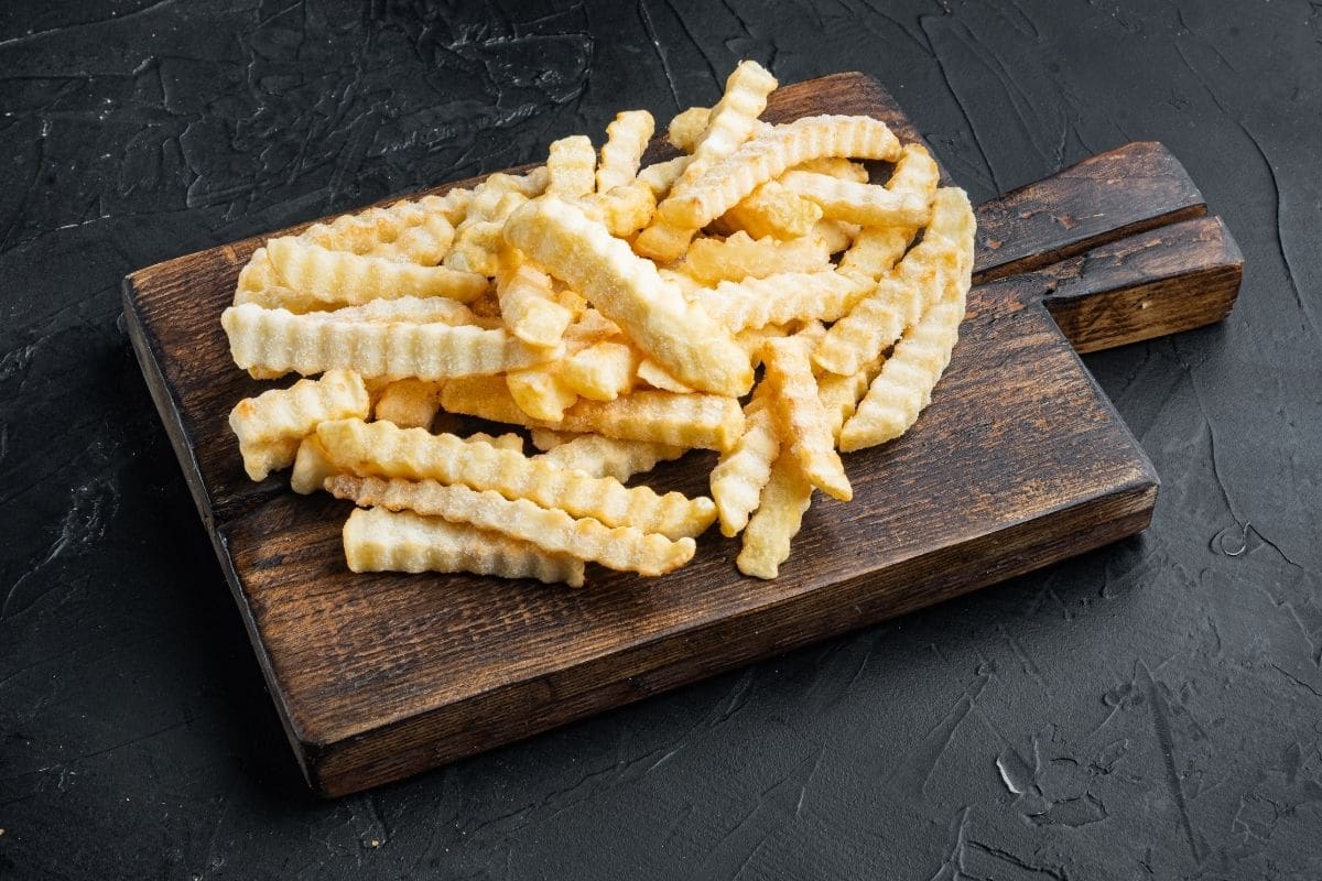 Frozen fries on wooden cutting board on a black table.