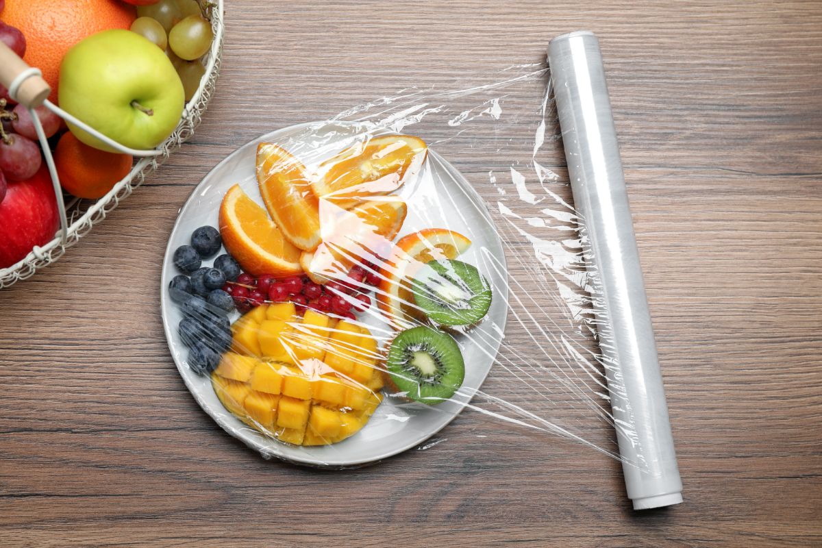 White plate full of fruit wrapped with plastic foil on table.