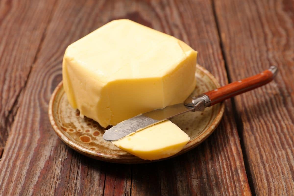 Block of buter on a small plate with knife on wooden table.