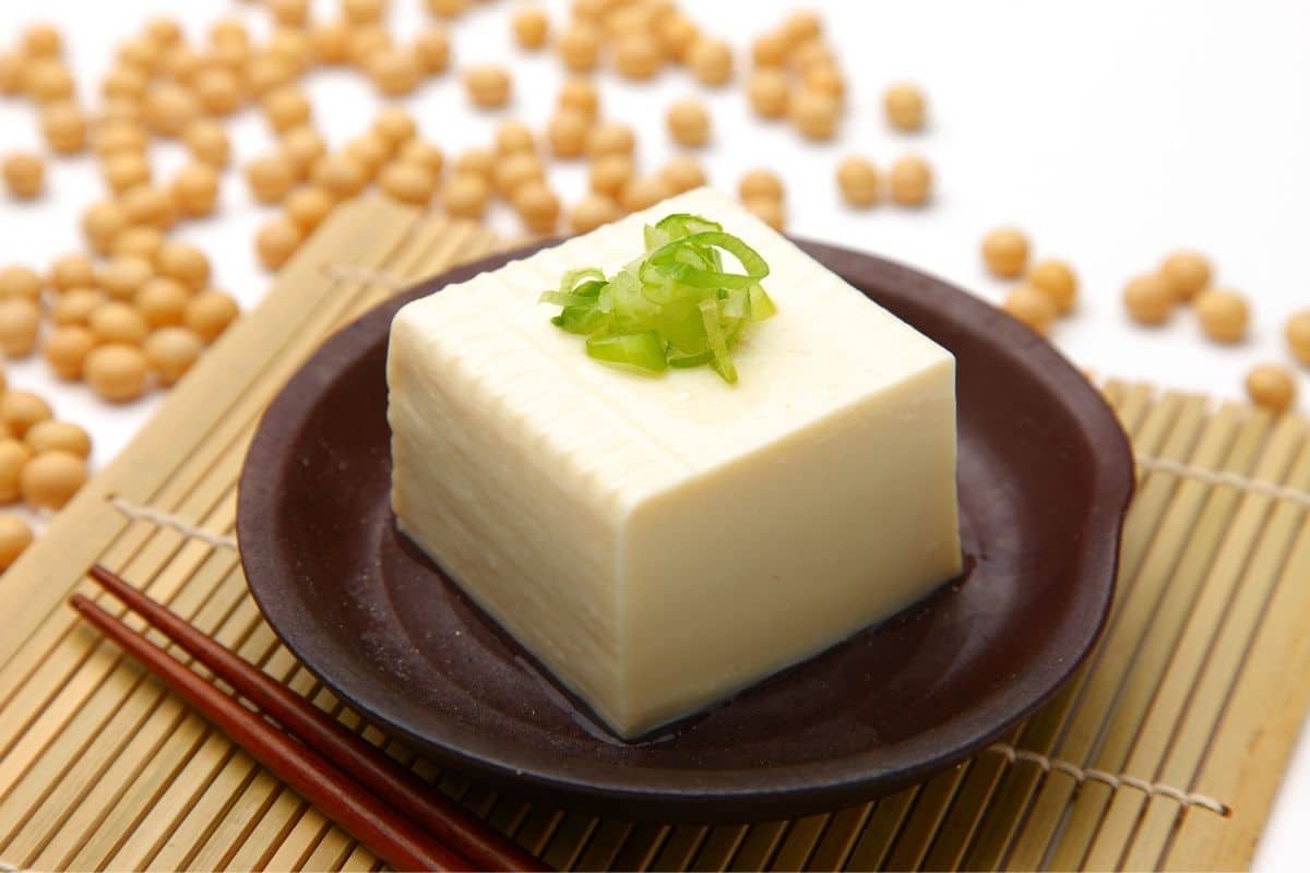 Block of tofu with herb on the top on brown plate on pad with sticks.