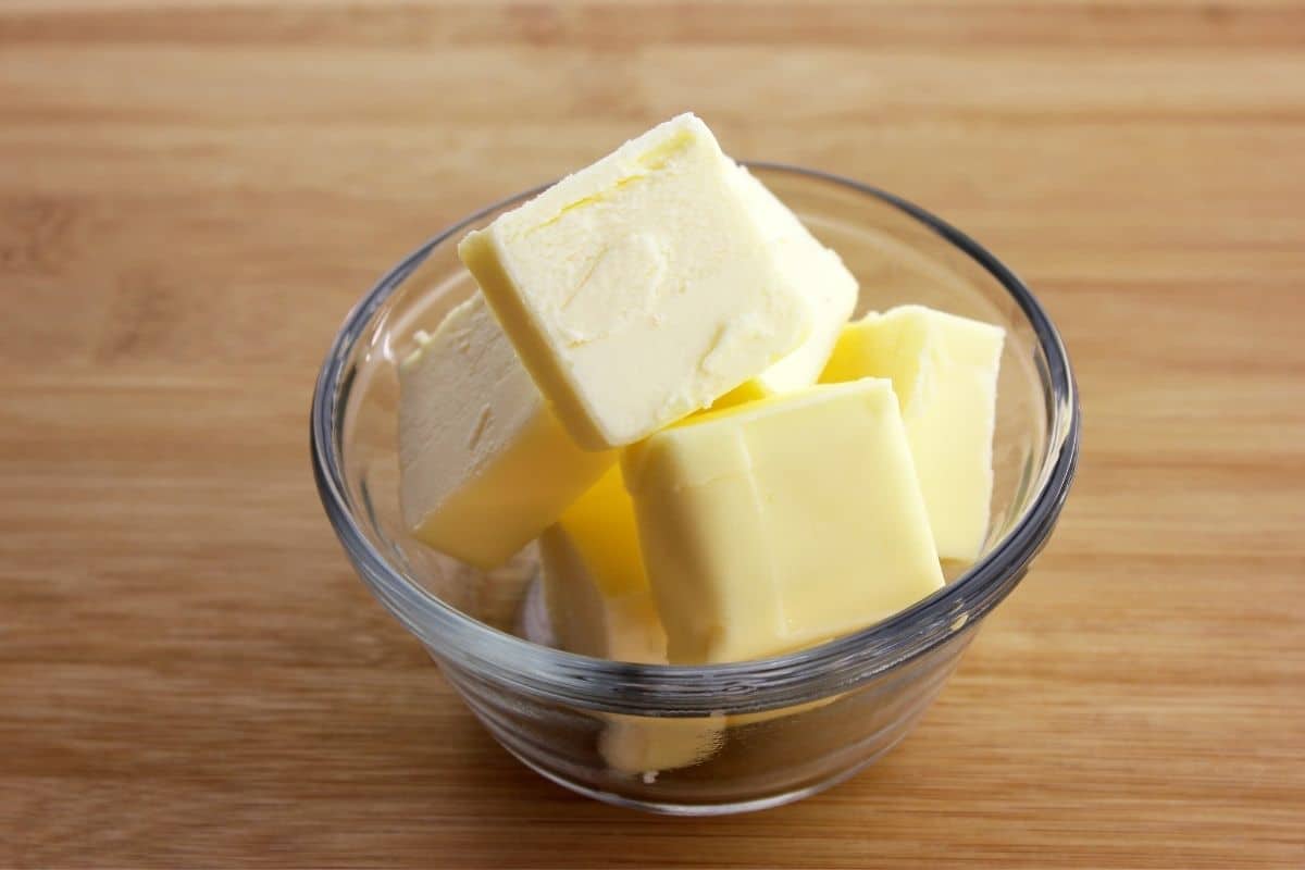 Small glass bowl full of block of butter on brown table.