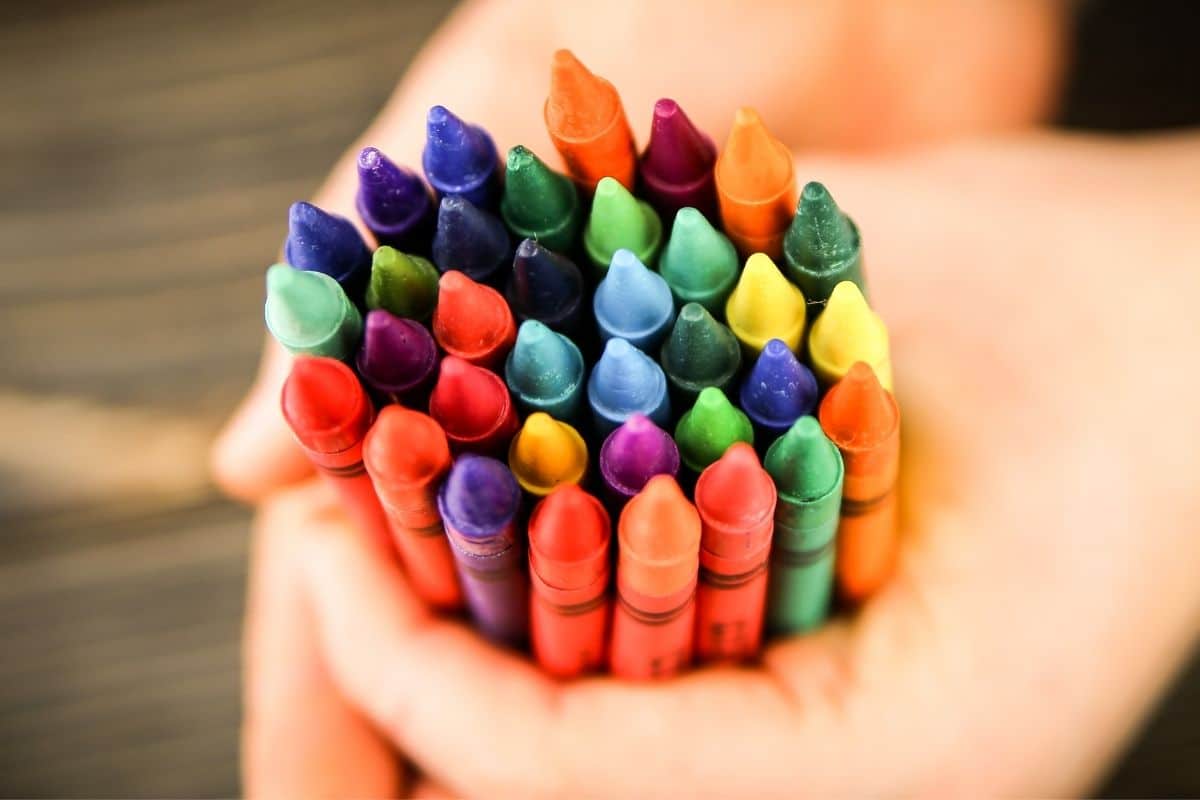 Hands holding bunch of colorful crayons.