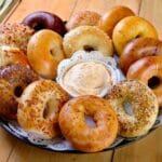 Tray full of bagels with bowl of dip on wooden table.