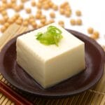 Block of tofu with herb on the top on brown plate.