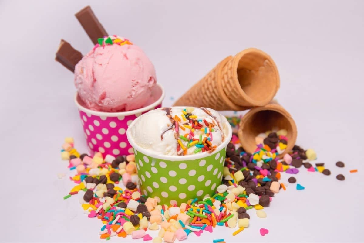 Ice cream in small cups with cones, sprinkles and chocolate chips scattered around.