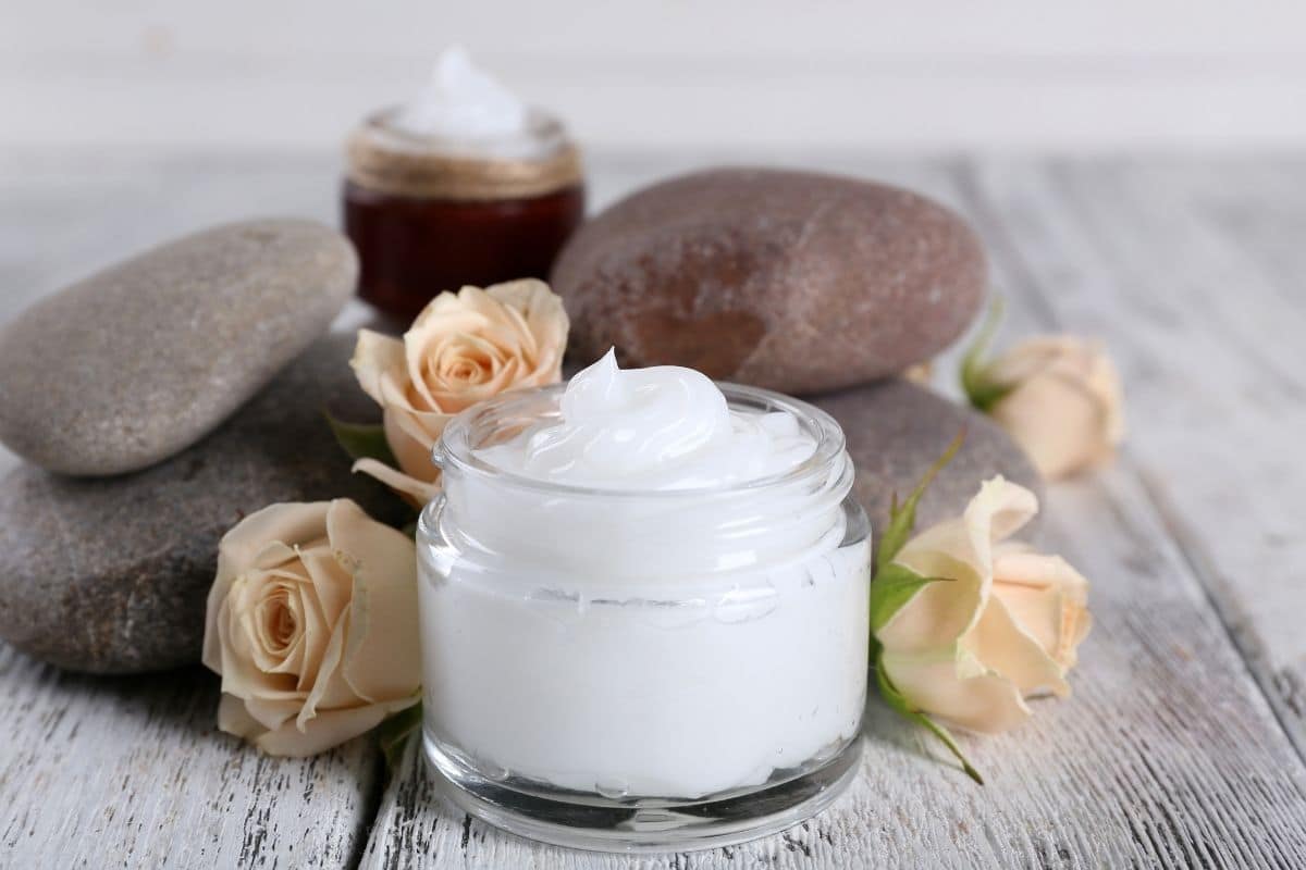 Glass jar full of lotion on table with rocks and roses.