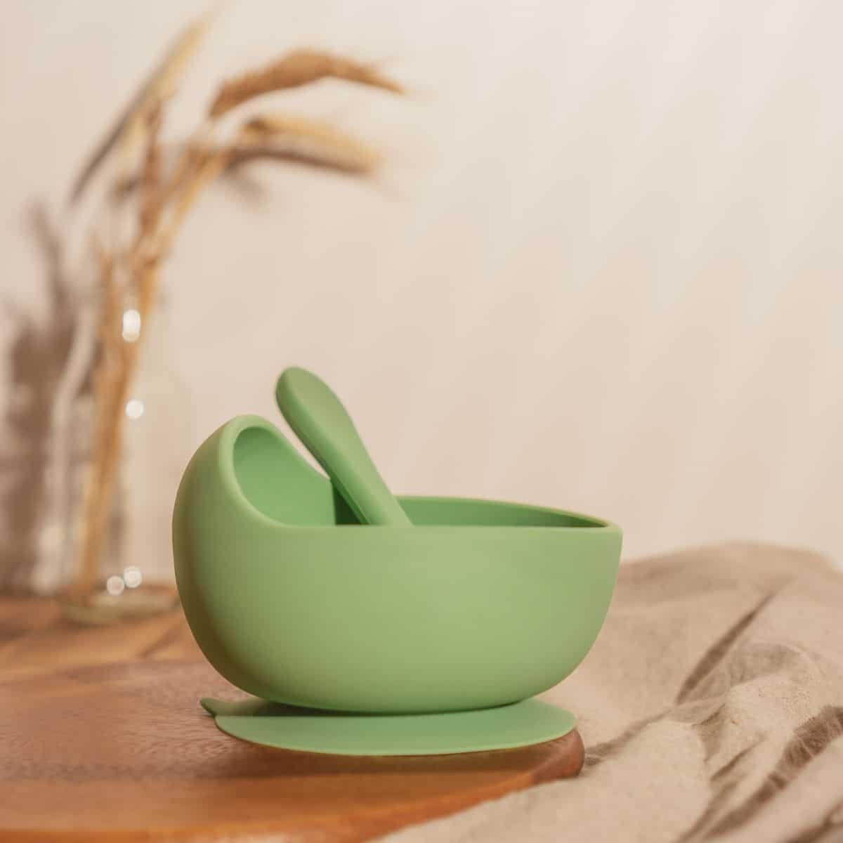 Modern green silicone bowl with spoon on wooden table.