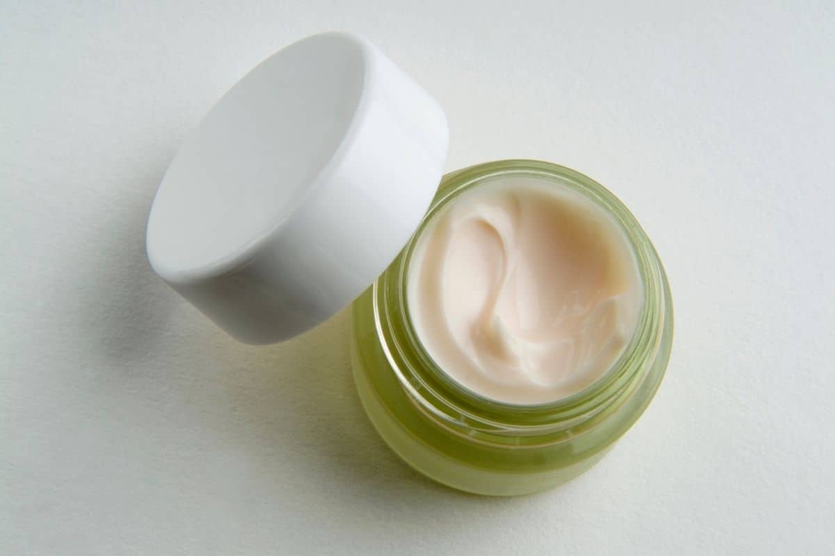 Green jar of lotion with white lid on white background.