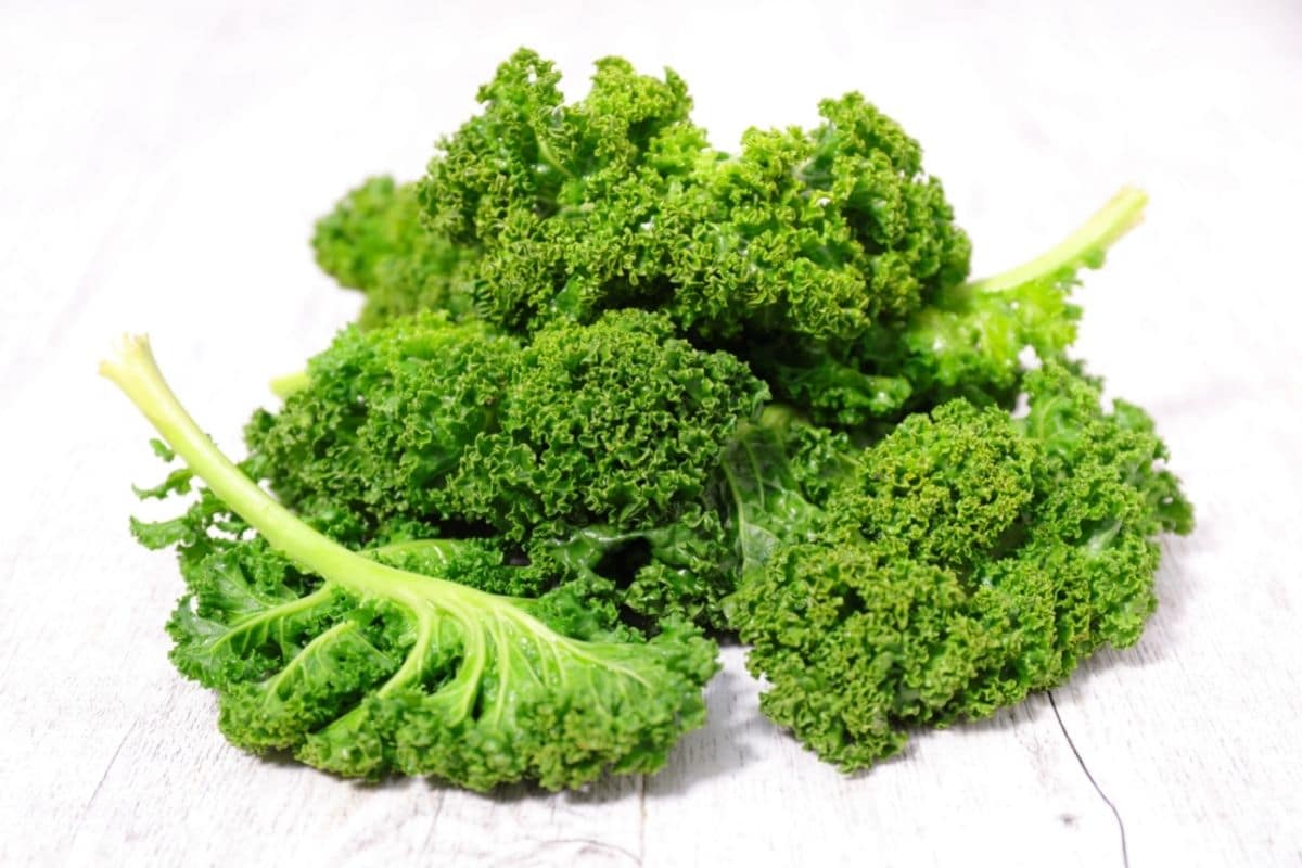 Fresh organic kale on white wooden table.