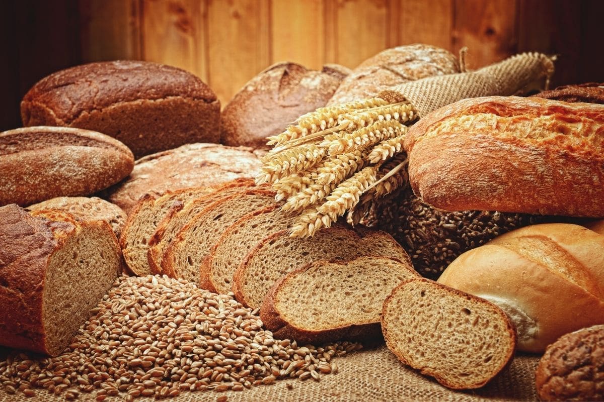Loeaves of bread, slices of bread, stalks of grain, scattered grains on table.