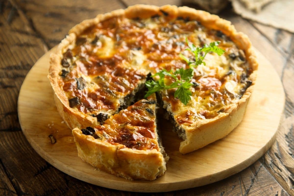 Whole homemade quiche on wooden board on wooden table.