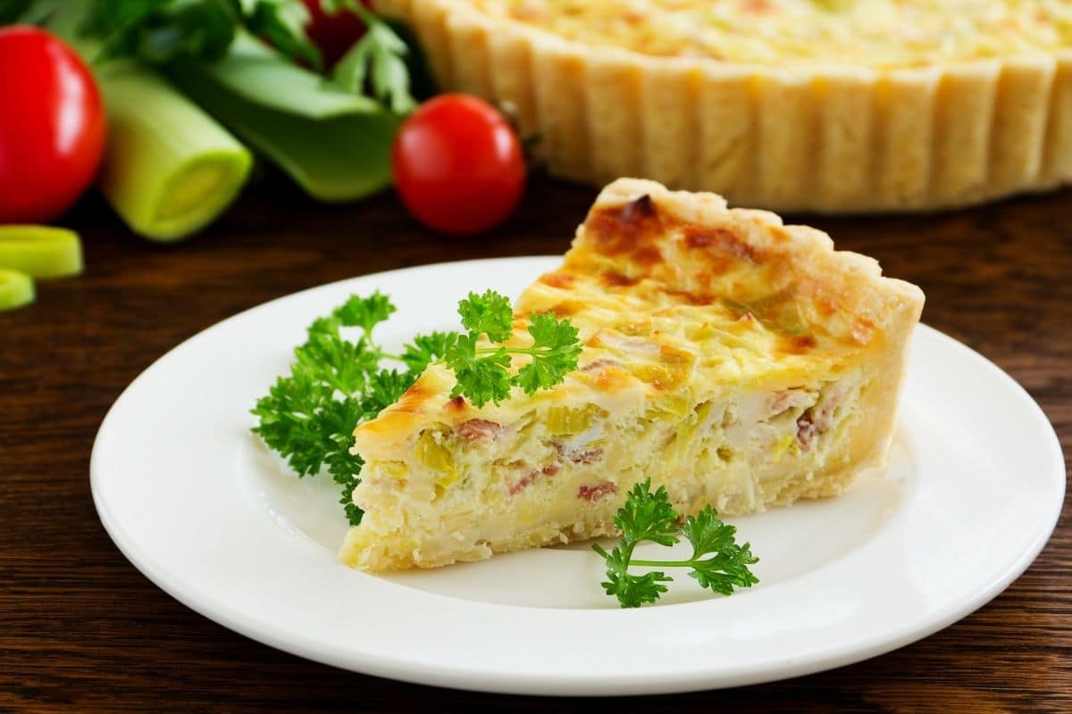 Slice of homemade quiche with herbs on white plate.