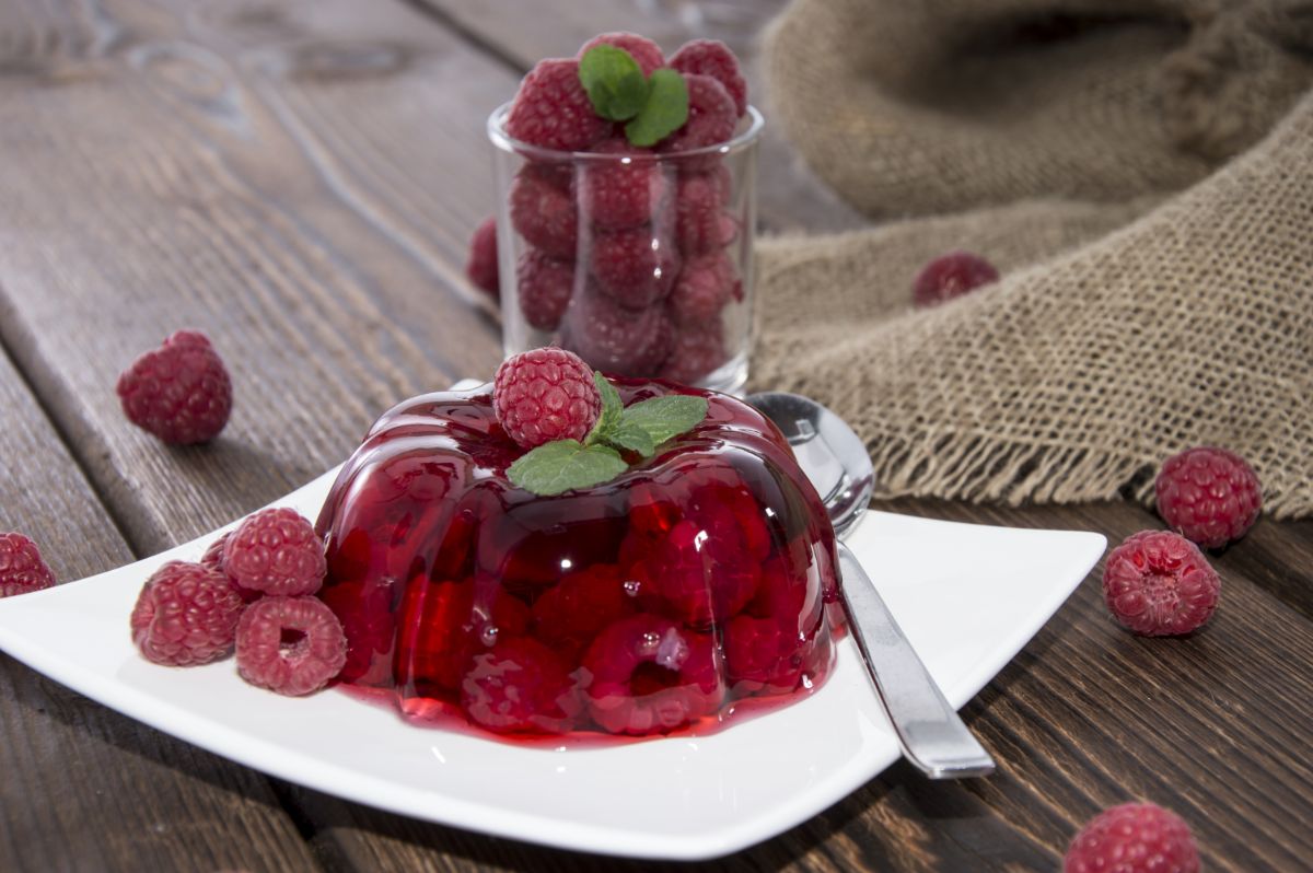 Raspberry jell-o on white plate with spoon on table with pack of raspberries.