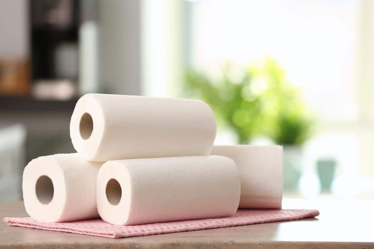 Three rolls of paper towels on pink cloth pad on kitchen table.