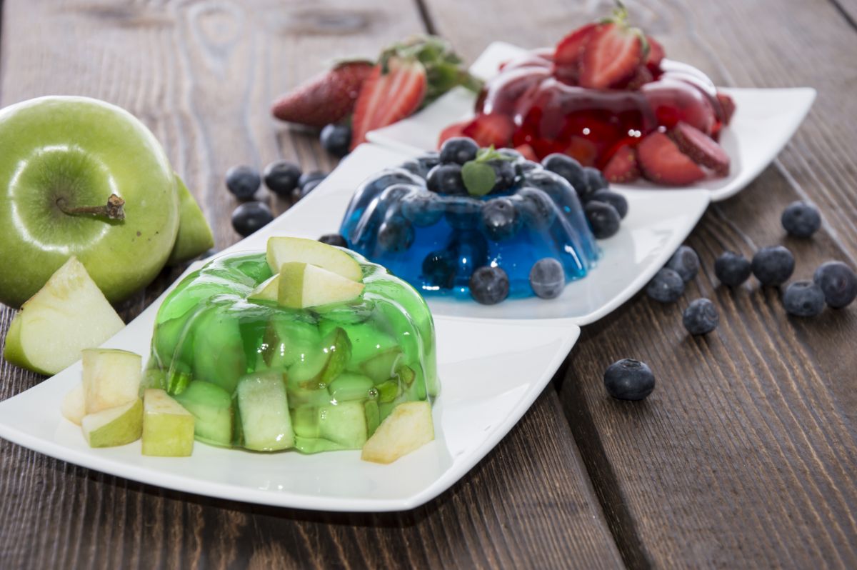 Apple, blueberry and strawberry jello-o on white plates on wooden table with fruits.