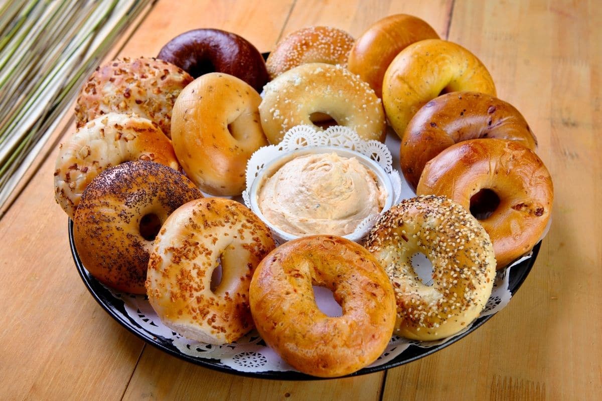 Tray full of bagels with bowl of dip on brown table.