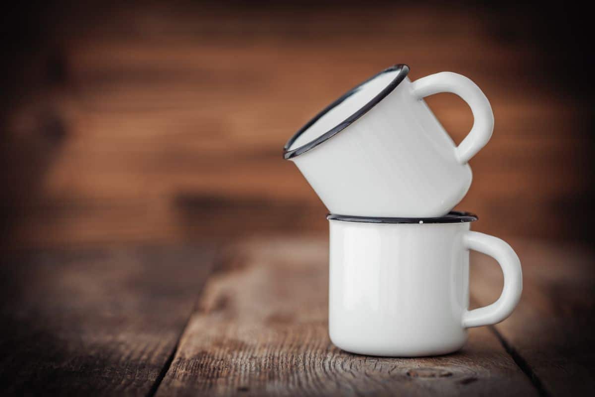 Two white enamel mugs on wooden table.