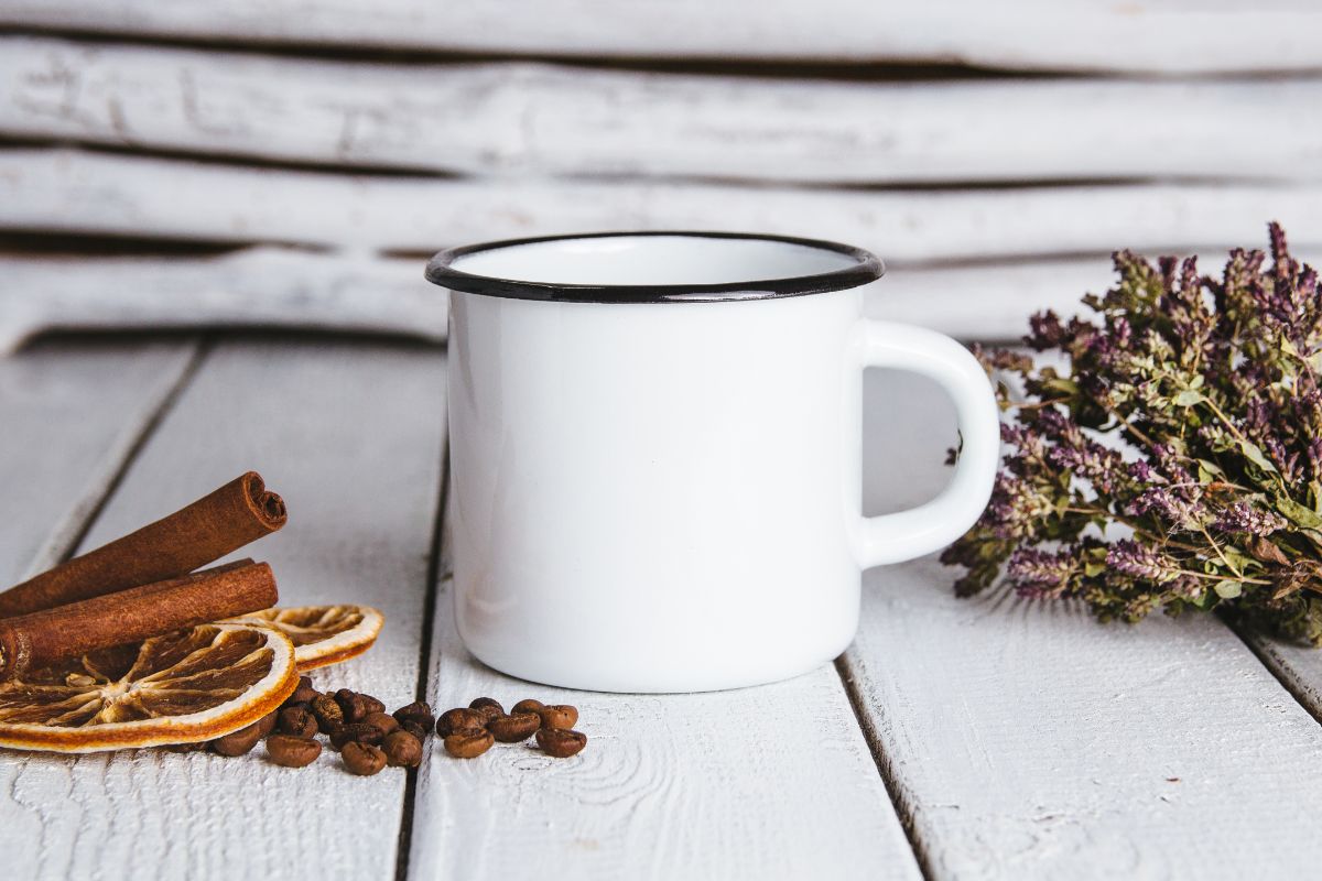 White enamel mug on white wooden table with herbs and ingredients around.