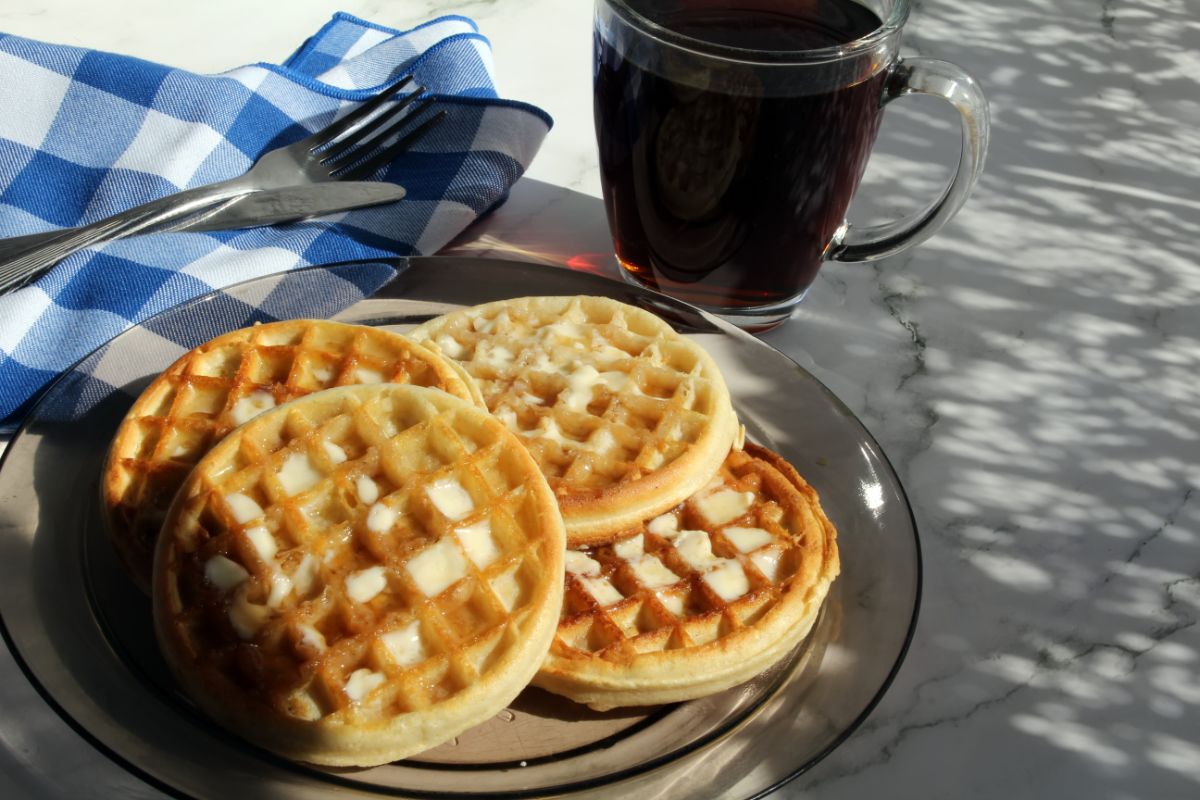 Eggo's waffles on glass tray on table with fork, cloth wipe and cup of coffe
