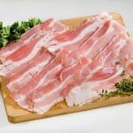 Stripes of bacon on wooden cutting board with herbs