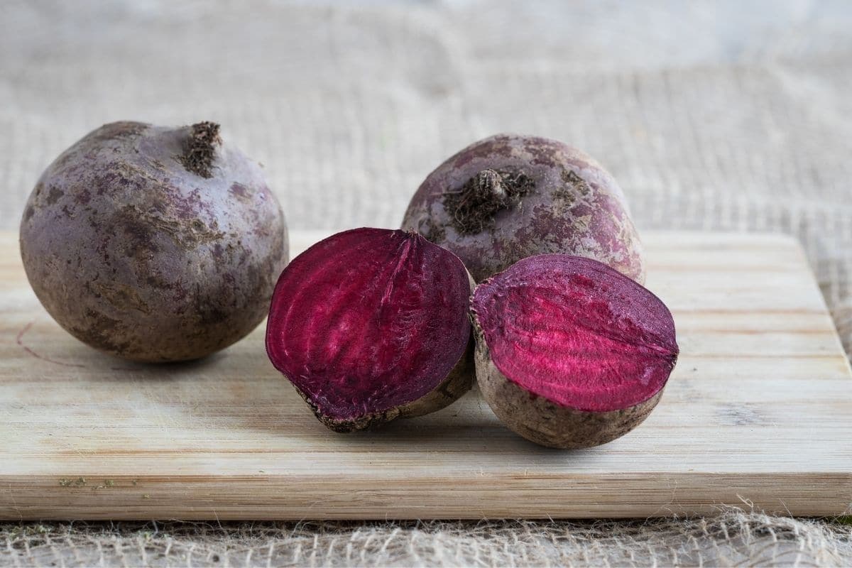 Whole and half cutted beets on wooden cutting board