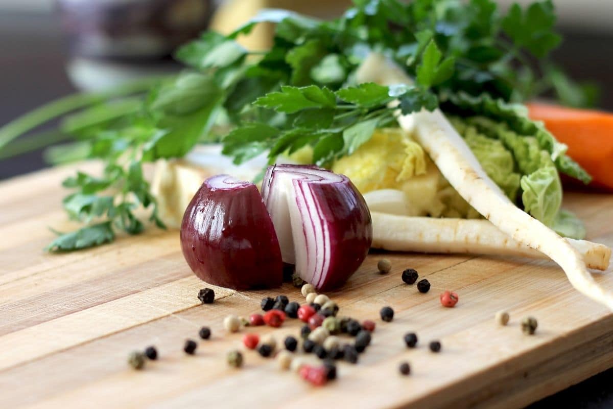 Two halfs of onion on wooden cutting board with vegetable and spicies.