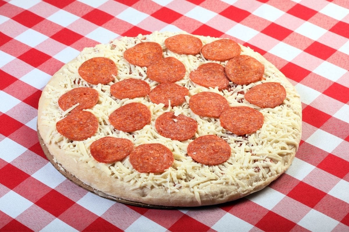 Frozen pizza on board on red-white table cloth.