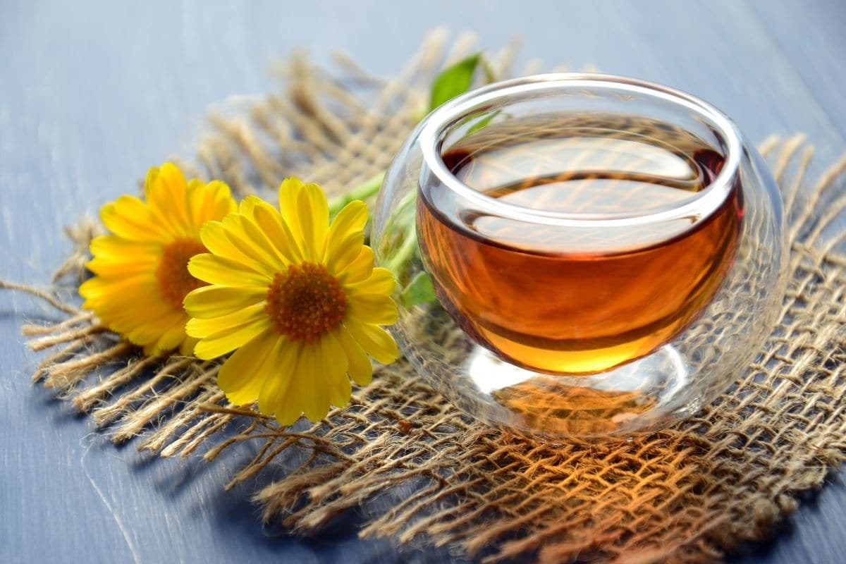 Glass jar of honey with yellow flowers, table cloth on black table