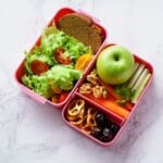 Pink lunch box full of fruits, vegetable and lunch dish